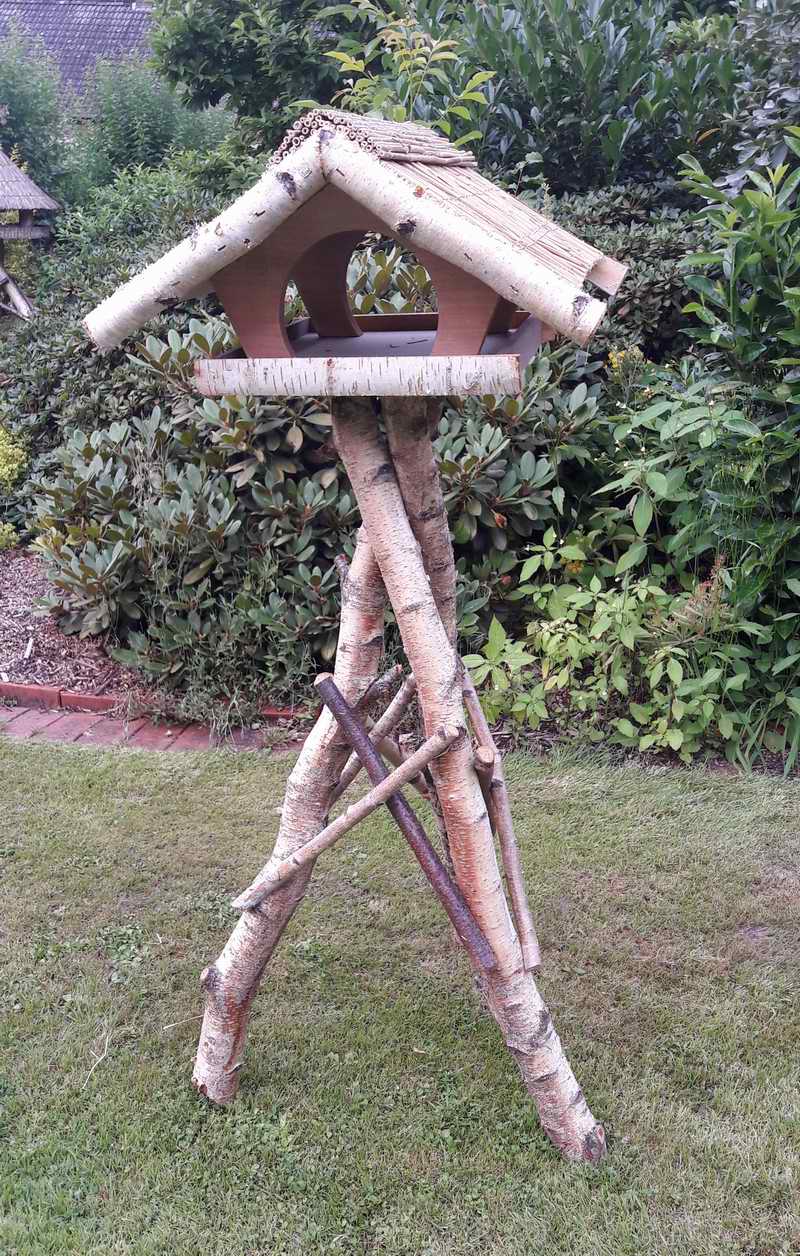 Vogelhaus mit Reetdach auf Birkenständer im Garten